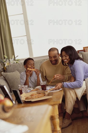 Family eating pizza in the living room. Photographe : Rob Lewine