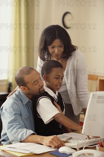 Boy and his parents looking at computer together. Photographe : Rob Lewine