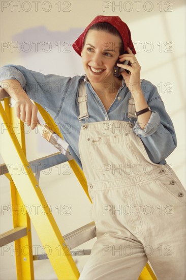 Woman talking on phone while painting her home. Photographe : Rob Lewine