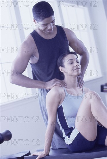 Man massaging woman's shoulders after a workout. Photographe : Rob Lewine