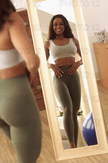 Woman admiring her flat stomach in a mirror. Photographe : Rob Lewine