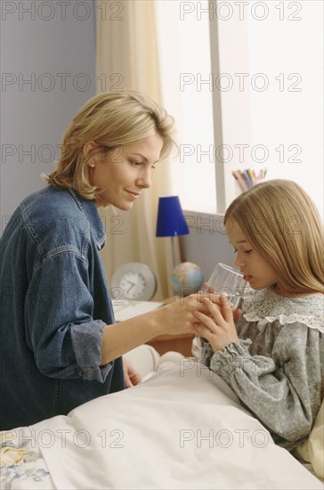 Mother giving sick daughter a drink of water. Photographe : Rob Lewine