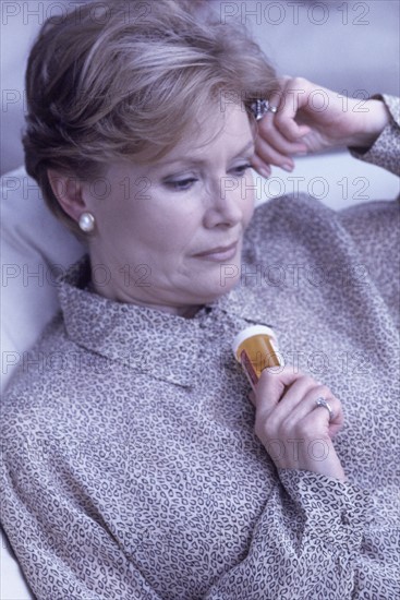 Depressed woman holding a bottle of prescription pills. Photographe : Rob Lewine