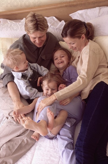 Family playing on bed together. Photographe : Rob Lewine