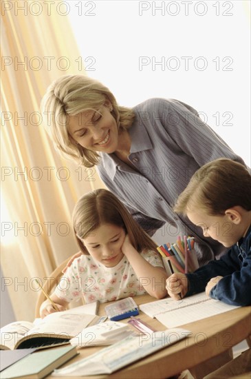 Mother watching her children coloring at the kitchen table. Photographe : Rob Lewine