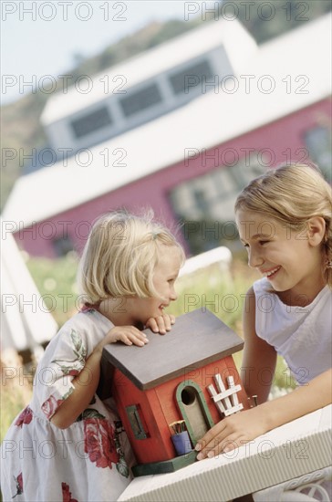 Siblings playing outdoors with a toy house. Photographe : Rob Lewine
