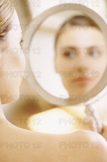 Woman looking at her reflection in a mirror. Photographe : Rob Lewine