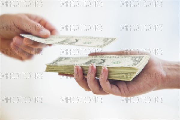 Hand putting dollar bill on top of stack of money.