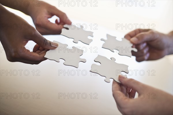 Four hands holding puzzle pieces.