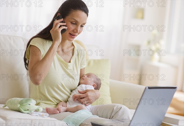 Mother talking on phone while holding her baby.