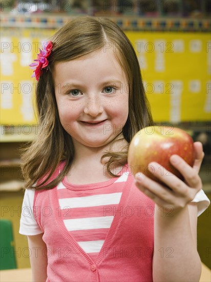 Kindergarten student holding an apple in classroom.