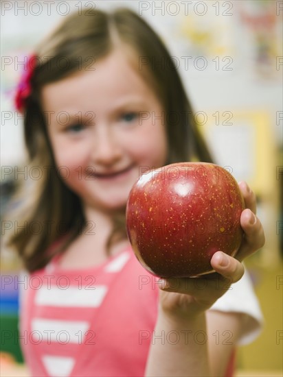 Kindergarten student holding an apple in classroom.