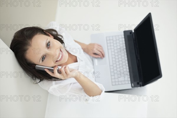 Woman talking on phone while working on laptop. Photo : momentimages