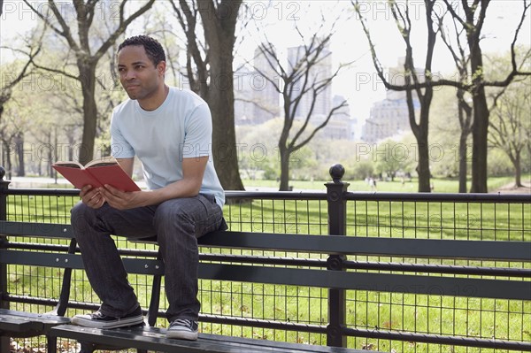 Man sitting on bench reading book in Central Park. Photo : David Engelhardt