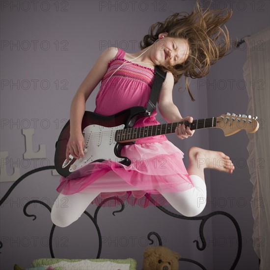 Young girls playing guitar on her bed. Photo : Mike Kemp