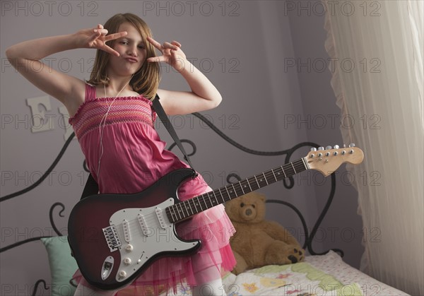 Young girls playing guitar on her bed. Photo : Mike Kemp