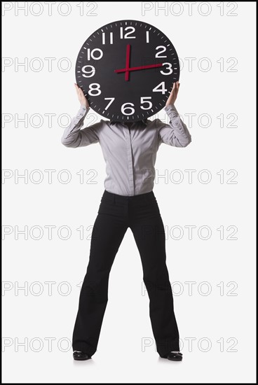 Businesswoman holding clock in front of her face. Photo : Mike Kemp