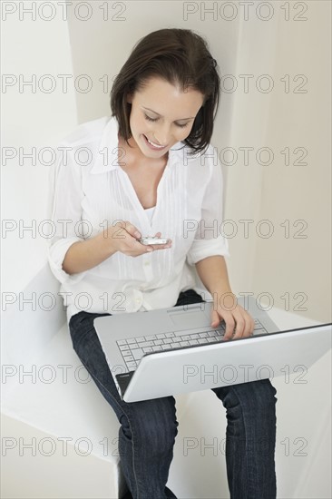 Woman texting while sitting with laptop. Photo : momentimages