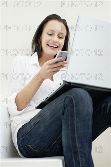 Woman texting while sitting with laptop. Photo : momentimages