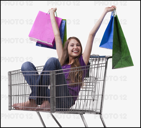 Excited woman sitting in a shopping cart with her purchases. Photo : Mike Kemp