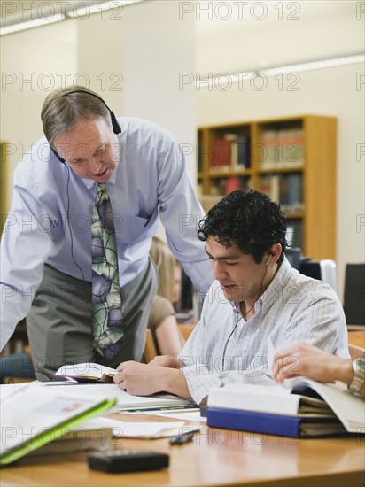 College professor helping college student in library.