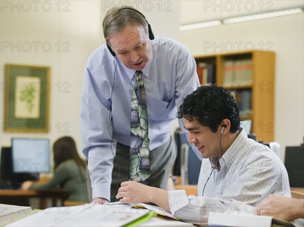 College professor helping college student in library.