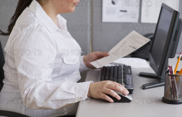 Businesswoman working on laptop in cubicle.