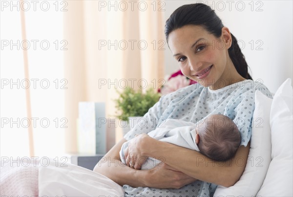 Mother holding newborn baby in hospital bed.