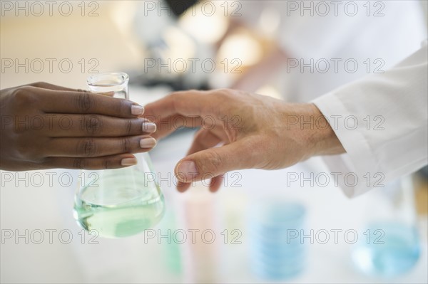 Hand passing beaker to another hand.