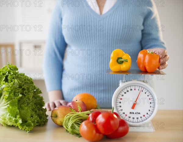 Overweight woman measuring peppers on a food scale.