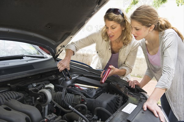Mother and daughter looking under hood of car.