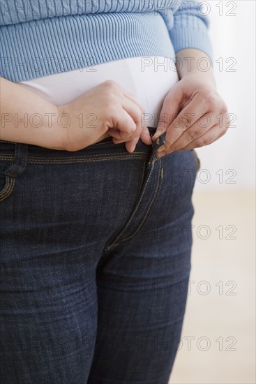 Overweight woman buttoning up her jeans.