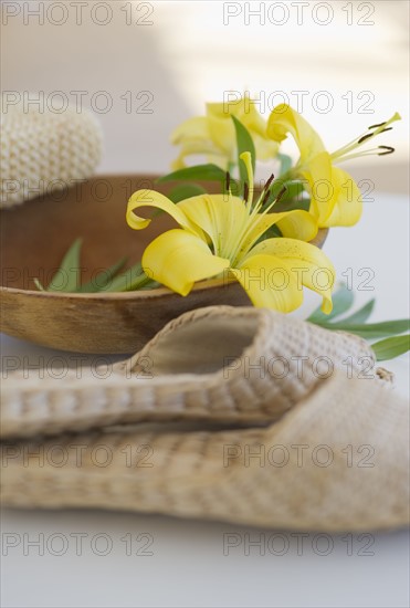 Slippers beside a wooden bowl with yellow lilies in it.