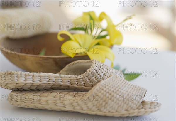 Slippers beside a wooden bowl with yellow lilies in it.