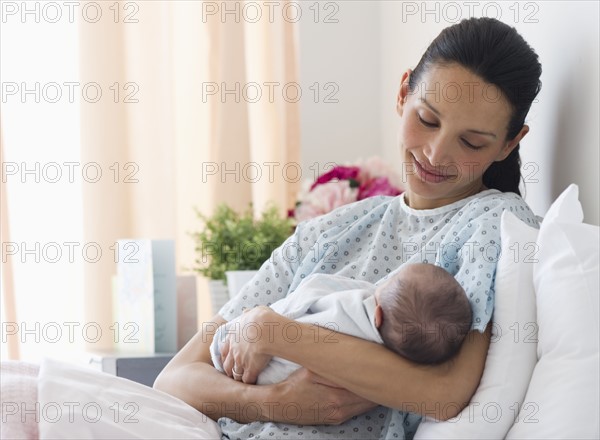 Mother holding newborn baby in hospital bed.