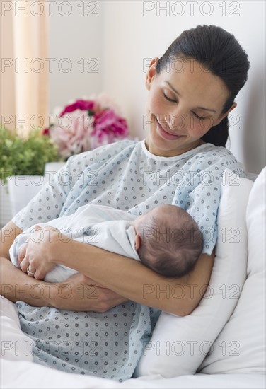 Mother holding newborn baby in hospital bed.