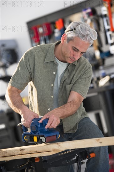 Handyman sanding a piece of wood in workshop.