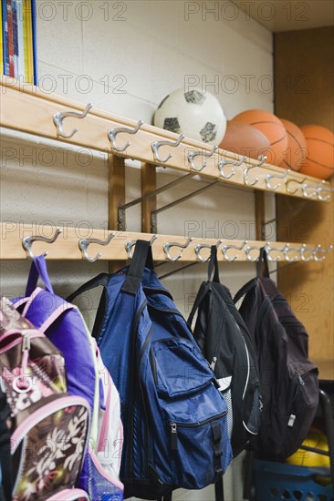 Children's backpacks hanging on hooks in classroom.