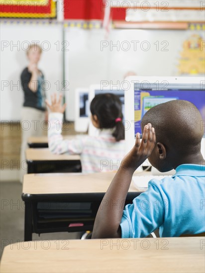 Elementary school students raising their hands in classroom.