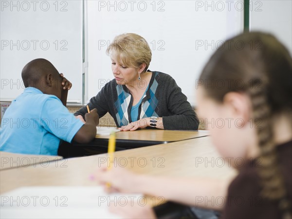 Teacher helping student in elementary school classroom.