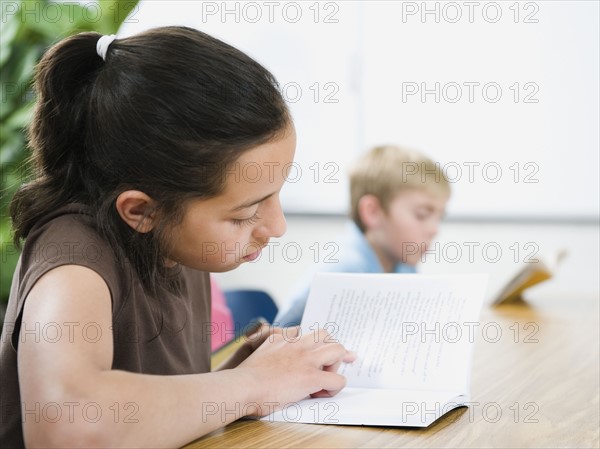 Elementary school students reading books at desk.