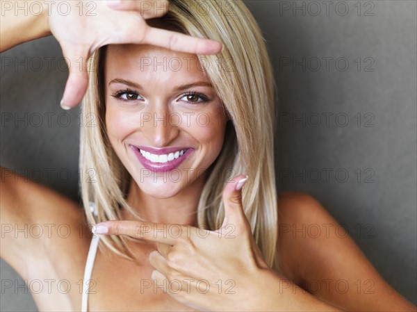 Blond woman making a hand frame around her face. Photo : momentimages