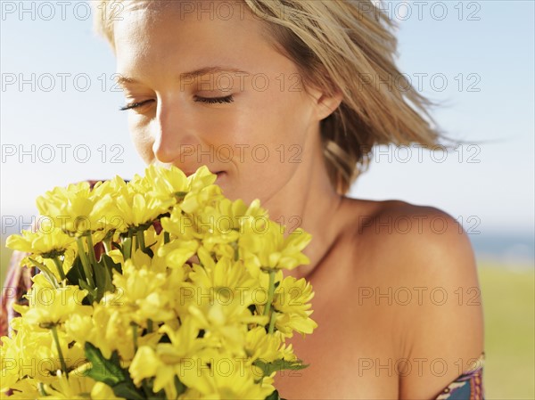 Blond woman smelling yellow flowers. Photo : momentimages
