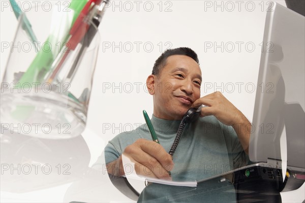 Man talking on phone while working on laptop. Photo : K.Hatt