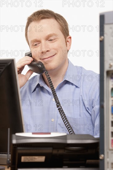 Businessman talking on phone while looking at computer. Photo : K.Hatt