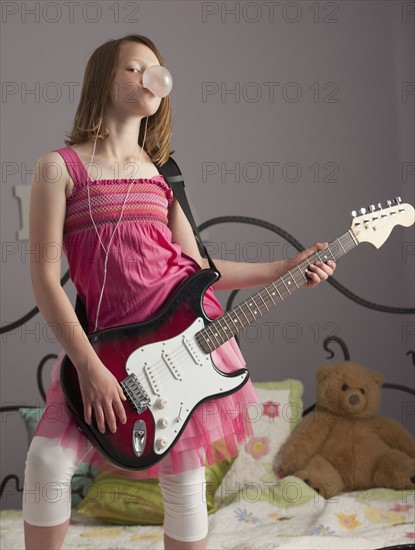 Young girls playing guitar on her bed. Photo : Mike Kemp