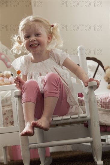 Young girl in rocking chair eating a sucker. Photo : Mike Kemp