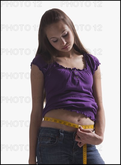 Upset teenage girl measuring her waist. Photo : Mike Kemp