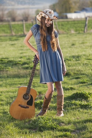 Long haired cowgirl holding guitar in field. Photo : Mike Kemp
