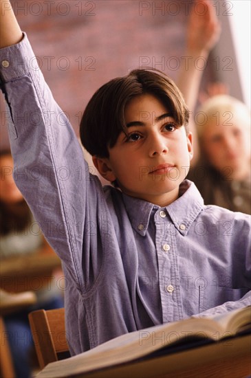 Elementary school student raising his hand in classroom. Photo : Rob Lewine